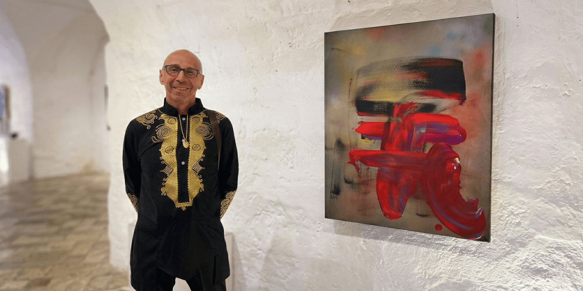 Marc Noël standing beside a vibrant abstract quantum painting at a contemporary art exhibition.