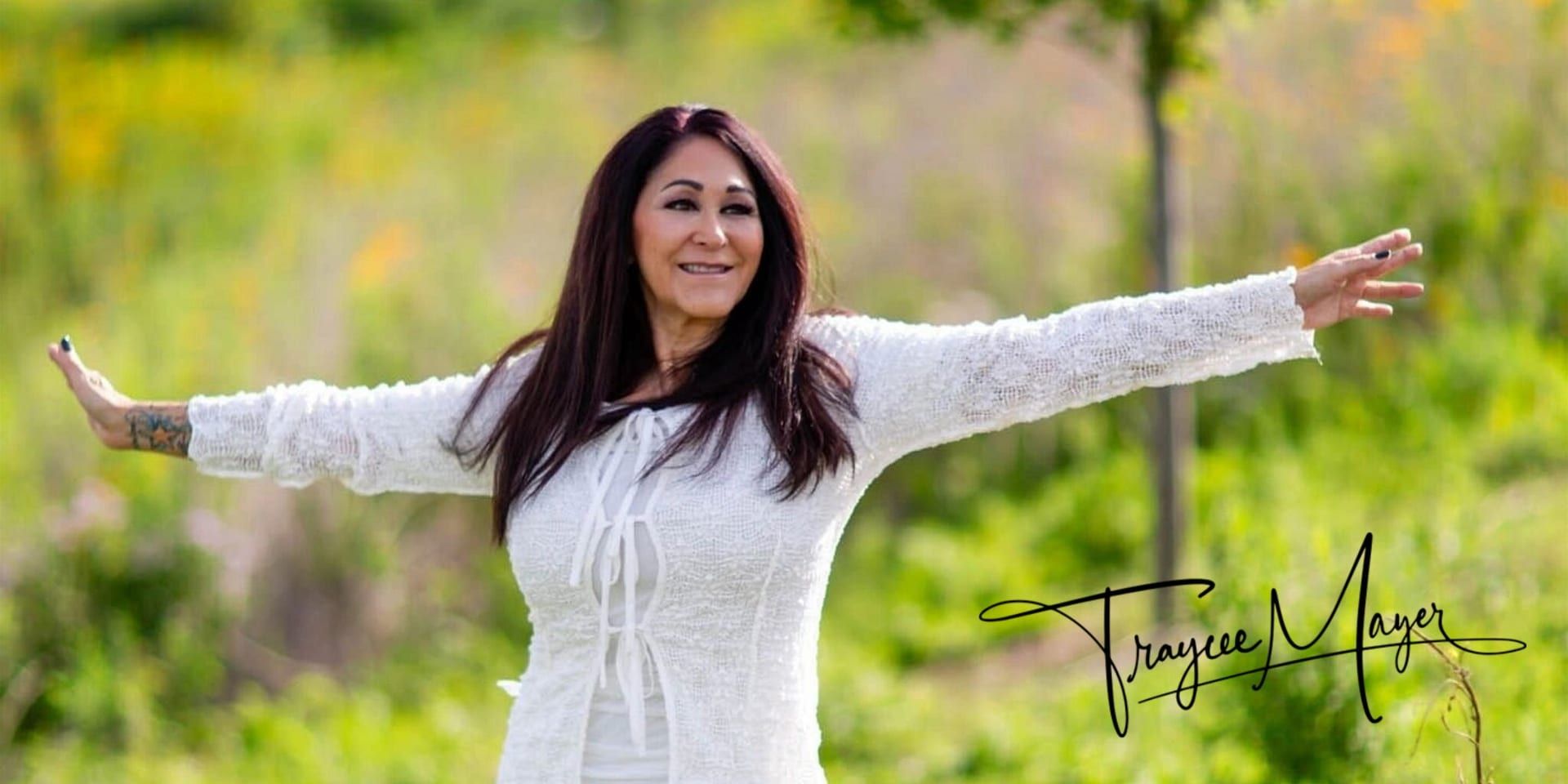 A woman stands in grass with arms outstretched, embodying openness and connection in a natural setting.