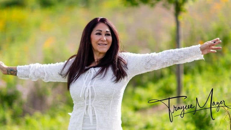 A woman stands in grass with arms outstretched, embodying openness and connection in a natural setting.