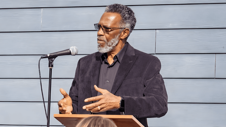 Man speaking at podium with microphone during community event, addressing audience about leadership, unity, and empowerment.
