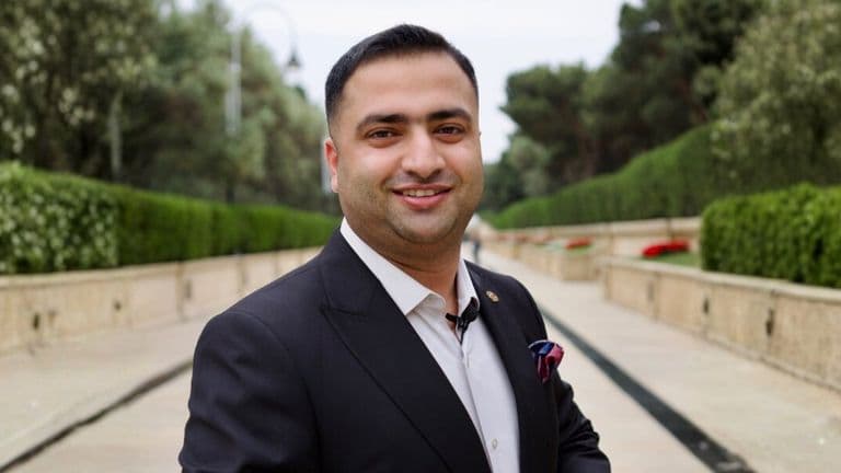 Dr. Hamza Tariq wearing a dark suit outdoors on a landscaped walkway.