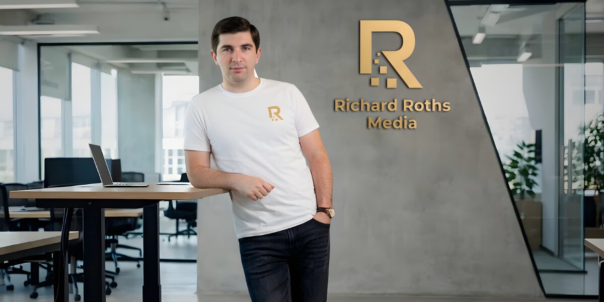 A person in a white shirt with a logo leans on a table in a modern office. The wall displays "Richard Roths Media" in gold. The atmosphere is professional.