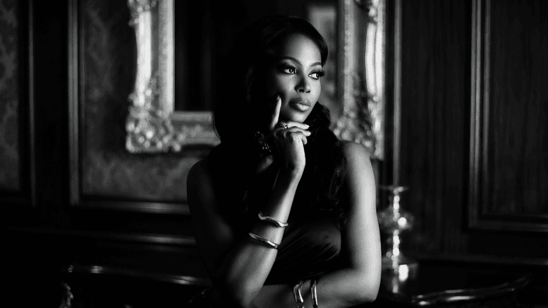 Elegant black-and-white portrait of woman in evening wear, posing thoughtfully in a refined interior setting.