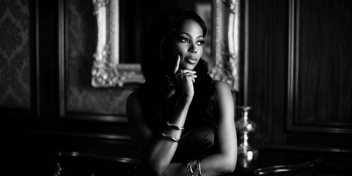 Elegant black-and-white portrait of woman in evening wear, posing thoughtfully in a refined interior setting.