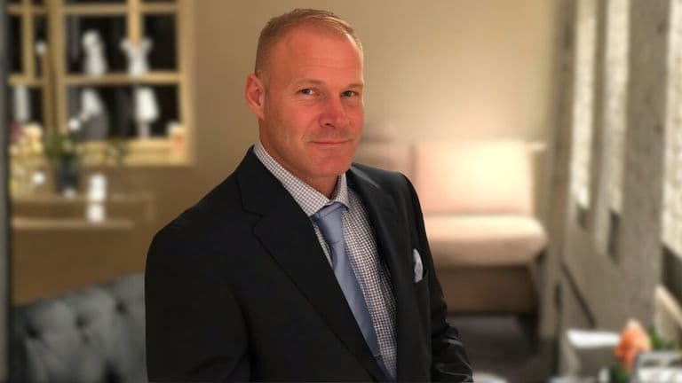 A man in a suit and tie stands thoughtfully in a room, embodying the mission of Beautiful Souls Inc. to inspire intentional living.