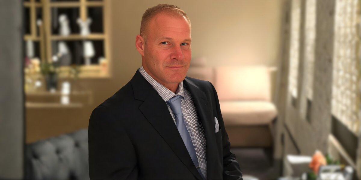 A man in a suit and tie stands thoughtfully in a room, embodying the mission of Beautiful Souls Inc. to inspire intentional living.