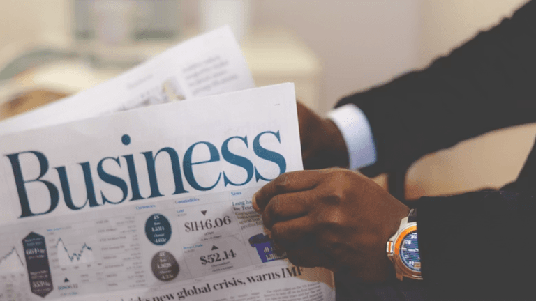 Person holding a business newspaper displaying financial charts and market information.