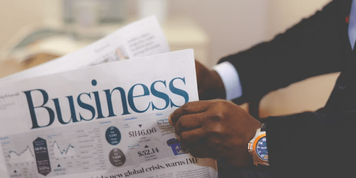 Person holding a business newspaper displaying financial charts and market information.