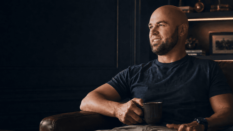 Veteran entrepreneur Adam Jacobs holding a coffee mug in a modern office, representing Astral & Root's wellness mission.