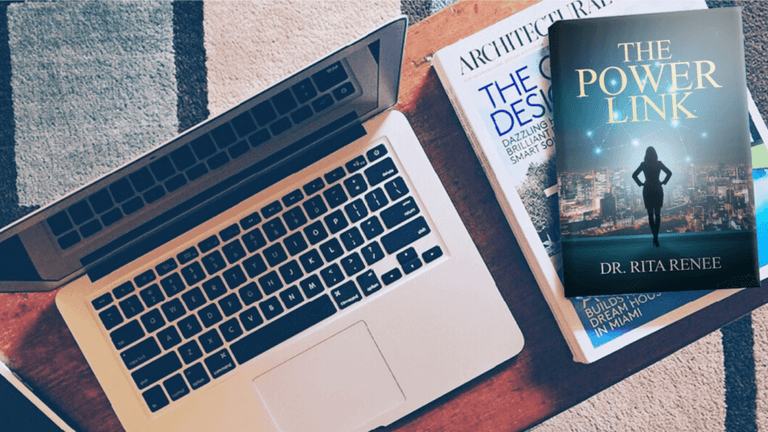 Laptop with architectural magazine and book titled 'The Power Link' by Dr. Rita Renee on a patterned rug, showcasing a modern business setup with a focus on professional development.