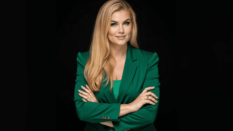 Portrait of a confident woman with blonde hair, wearing a green blazer, standing with her arms crossed against a dark background. She exudes a professional and empowering presence, embodying the essence of leadership and growth in line with Happy Life Academy’s mission.