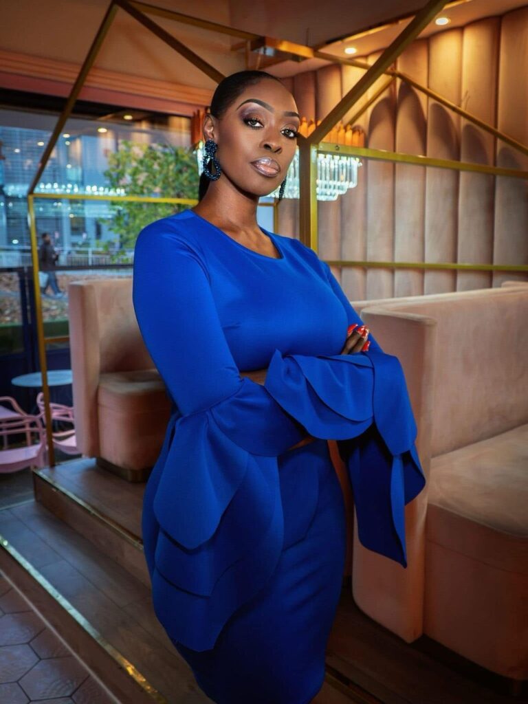 Dilys Sillah standing with folded arms in a blue dress inside a modern lounge.